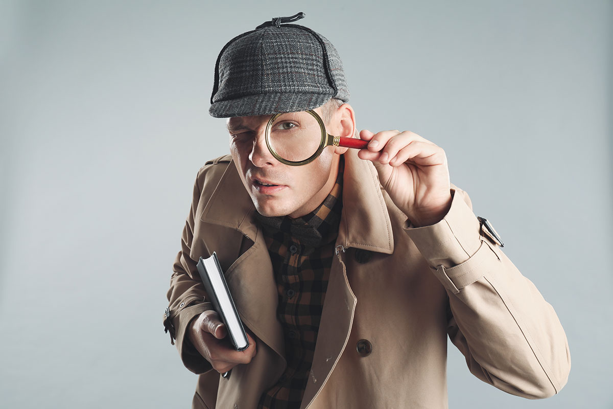 Plagiarism detective! Man dressed in an old fashioned detective outfit with a magnifying glass to his eye